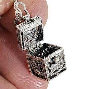 May include: A silver charm necklace featuring a small, open, ornate box pendant. The box is hinged and has a detailed design.
