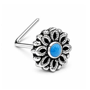 Può includere: Un piercing al naso argentato con un design floreale e dettagli intricati. Il centro del fiore contiene una pietra rotonda blu chiaro. Il piercing ha un perno a forma di L.
