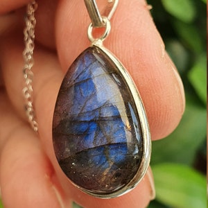 May include: A silver pendant with a teardrop-shaped labradorite gemstone. The stone has a blue and purple iridescent sheen.
