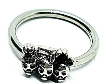 Può includere: Anello d'argento con un design a tre teschi. I teschi sono dettagliati e hanno un'estetica leggermente gotica.
