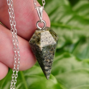 May include: A silver chain necklace with a green and black gemstone pendant in the shape of a point.