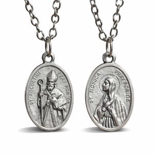 May include: Two silver-coloured oval pendants on chains. One pendant features St. Augustine with a staff, the other St. Monica. Both pendants have the words "PRAY FOR US" and the saint's name engraved around the edges.