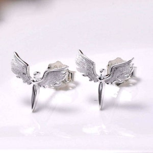 May include: A pair of silver angel wing earrings. The angel wings are detailed and have a textured finish. The earrings are a simple stud style.