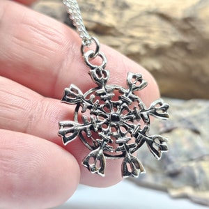 May include: Silver snowflake pendant necklace with a black centre stone. The snowflake is detailed and intricate.