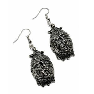 May include: A pair of silver-colored earrings. Each earring features a detailed, stylized face with a hat. The earrings have a hook closure.
