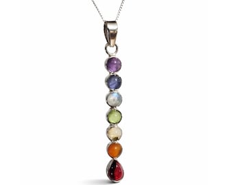 May include: A vertical silver pendant necklace featuring seven round, multi-colored gemstones arranged in a column, topped with a silver bail and suspended from a thin silver chain. The stones display a gradient of purple, blue, white, green, yellow, orange, and a teardrop-shaped red stone at the base.