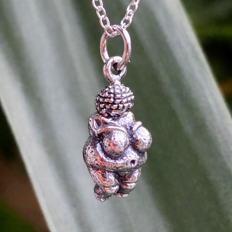 Puede incluir: Un collar con colgante de plata con una peque&ntilde;a y detallada escultura de la Venus de Willendorf. El colgante est&aacute; suspendido de una delicada cadena de plata. La escultura representa una figura femenina estilizada y curvil&iacute;nea.