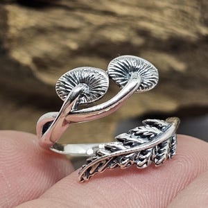 May include: A silver ring featuring a mushroom and fern design. The ring is adjustable and can be worn on any finger.