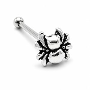 May include: A silver-toned barbell body jewellery piece featuring a detailed spider charm at one end. The spider has a polished, rounded body and eight legs, with darkened recessed areas to highlight the texture of the metal design on a plain background.