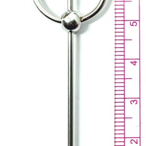 May include: A silver-colored body piercing jewelry piece. The design features a central spike, two curved spikes, and a central ball. The piece measures approximately 8 cm in length.