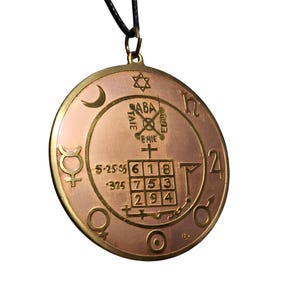 May include: A copper-colored pendant with a black cord. The round pendant features etched symbols, numbers, and text within concentric circles. A six-pointed star and crescent moon are visible. The pendant is approximately 2 inches in diameter.
