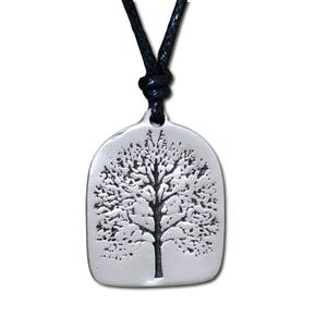 May include: A silver-colored pendant necklace featuring a detailed tree design. The pendant is rectangular with rounded edges and hangs from a black cord. The tree's branches and trunk are intricately etched into the metal.