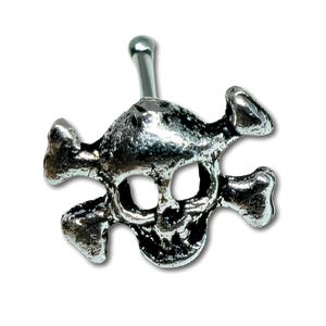 Könnte beinhalten: Ein silberfarbener Bauchnabelpiercing mit einem Totenkopf- und gekreuzten Knochen-Design. Der Totenkopf hat detaillierte Gesichtszüge, und die gekreuzten Knochen befinden sich hinter dem Totenkopf. Der Ring hat einen gebogenen Stab mit einer kleinen Kugel oben.