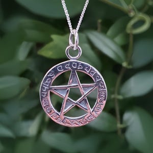 May include: A silver pendant necklace with a pentagram charm. The pentagram is surrounded by a circle with an inscription in an ancient language.