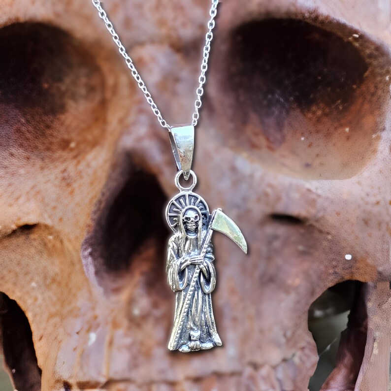 Pu&ograve; includere: Collana d'argento con un ciondolo dettagliato di una figura scheletrica che tiene una falce. Il ciondolo ha la forma di una persona che indossa una tunica.