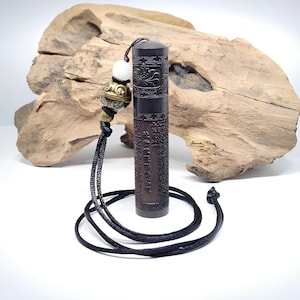 Puede incluir: Un colgante cilíndrico de madera marrón oscuro con intrincados tallados y caracteres chinos. El colgante está unido a un cordón negro con una cuenta blanca y una cuenta dorada con un diseño decorativo.