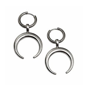 May include: A pair of silver-colored crescent moon earrings. Each earring features a small hoop at the top, connected to a larger, curved crescent shape. The earrings are displayed against a white background, highlighting their metallic sheen and minimalist design.
