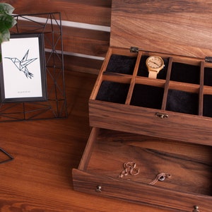 May include: A wooden jewelry box with a drawer and a top compartment with multiple slots for storing watches. The box is made of dark wood with a natural wood grain. The top compartment is lined with black velvet. A watch is visible in one of the slots.