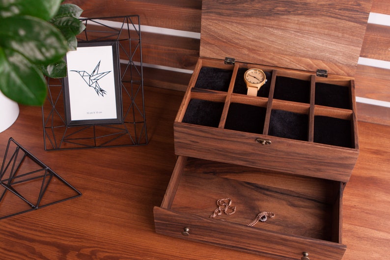 May include: A wooden jewelry box with a drawer and a top compartment with multiple slots for storing watches. The box is made of dark wood with a natural wood grain. The top compartment is lined with black velvet. A watch is visible in one of the slots.
