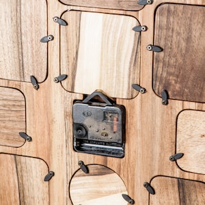 May include: A wooden clock with a round face and a clock mechanism visible on the back. The clock has a unique design with multiple rectangular openings around the clock face.
