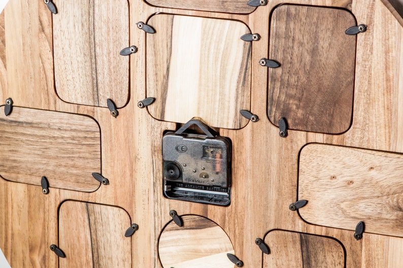 May include: A wooden clock with a round face and a clock mechanism visible on the back. The clock has a unique design with multiple rectangular openings around the clock face.