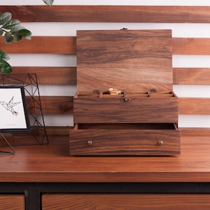 May include: A wooden jewelry box with a hinged lid and a drawer. The box has a dark brown finish and is made of wood. The box has compartments for storing jewelry and other small items.