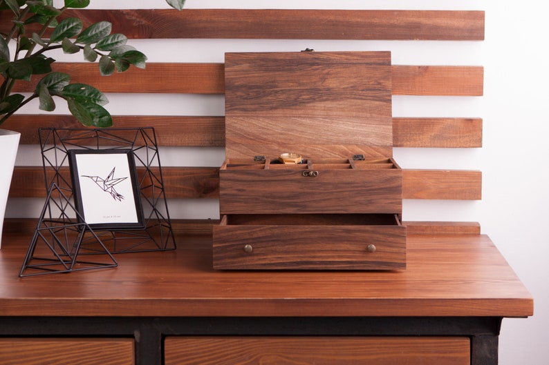 May include: A wooden jewelry box with a hinged lid and a drawer. The box has a dark brown finish and is made of wood. The box has compartments for storing jewelry and other small items.