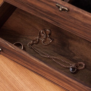 May include: A wooden jewelry box with a drawer open, revealing a gold necklace with a black gemstone pendant and a gold ring.
