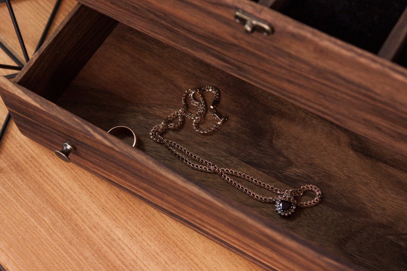 May include: A wooden jewelry box with a drawer open, revealing a gold necklace with a black gemstone pendant and a gold ring.