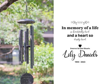 May include: A black metal wind chime with a round, engraved tag that reads "In memory of a life so beautifully lived and a heart so deeply loved. Forever in our hearts, Lily Daniels, 1955-2023".