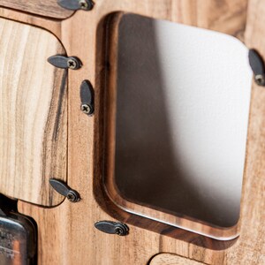 May include: Close-up of a wooden clock face with a metal clock mechanism. The clock face has a rectangular opening with a beveled edge. The clock is made of light brown wood with dark brown accents.