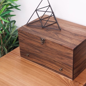 May include: A dark brown wooden box with a metal latch and decorative metal accents. The box is sitting on a light brown wooden surface.