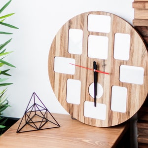 May include: A round wooden clock with 12 square picture frames. The clock has a black hour hand and a red minute hand. The clock is on a wooden table next to a black metal geometric sculpture.