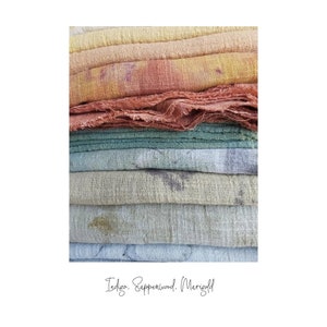 May include: A stack of colorful, textured fabric in shades of yellow, orange, green, and blue. The fabric appears to be hand-dyed, with visible variations in color and texture. The text "Indigo. Sappperwood. Marigold" is written in cursive at the bottom.