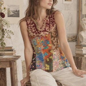 May include: A sleeveless top featuring a patchwork design with various colourful floral and abstract patterns. The neckline is accented with cream-coloured lace trim. The garment is constructed from multiple fabric panels joined by visible stitching.