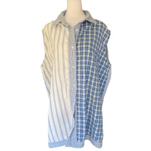 Op de afbeelding: Mouwloos overhemd met patchwork-ontwerp. De ene kant heeft verticale blauwe strepen op een witte achtergrond, de andere een blauw-wit ruitpatroon. Het heeft een klassieke kraag en een knoopsluiting. Een mix van patronen.