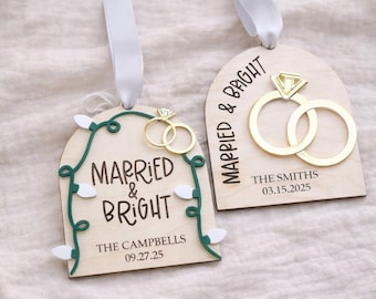 May include: Two arched wooden ornaments with white ribbon hangers. One features a green string of lights, the text "MARRIED & BRIGHT", and "THE CAMPBELLS 09.27.25". The other shows two gold rings, "MARRIED & BRIGHT", and "THE SMITHS 03.15.2025".