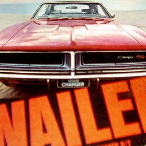 May include: A red 1969 Dodge Charger with a black grille and chrome bumpers. The car is parked on a beach with the word "WAILER" in large red letters in the foreground.