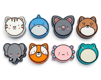 May include: A set of eight colorful animal-shaped silicone stamps or coasters featuring cartoon faces of a tiger, shark, bat, dog, elephant, fox, axolotl, and frog, each with distinct facial features and vibrant color palettes.