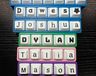 May include: A collection of custom keyboard keycaps spelling out names. The names include Zahara, Dawes, Joshua, Dylan, Talia, and Mason. Each name is displayed on a different colored frame: blue, green, pink, and purple.