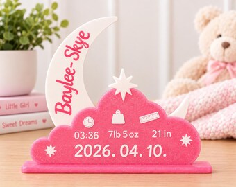 May include: A pink and white acrylic birth announcement sign shaped like a crescent moon and a cloud. The sign features the name Baylee-Skye, the birth time 03:36, weight 7lb 5oz, length 21 in, and the date 2026. 04. 10. with star and icon accents.