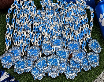 May include: A collection of blue and white plastic chain necklaces, each featuring a shield-shaped pendant with a blue lion graphic and the text BRICK CITY LIONS. The pendants are arranged in a cluster, showcasing the team-themed sports memorabilia.