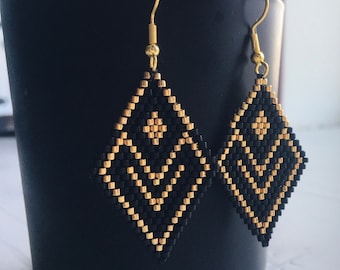 Può includere: Un paio di orecchini geometrici neri e dorati a forma di diamante. Gli orecchini sono realizzati con piccole perline e hanno un gancio dorato.