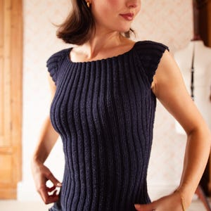 Könnte beinhalten: Ein marineblaues Rippstrick-Top mit quadratischem Ausschnitt und kurzen Ärmeln. Das Top hat eine figurbetonte Silhouette und vertikale Rippendetails. Das Model trägt goldene Creolen und ein goldenes Armband.