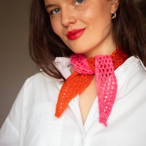 Peut inclure: Une femme portant une chemise blanche boutonnée avec une écharpe en crochet dans les tons rose et orange autour du cou.