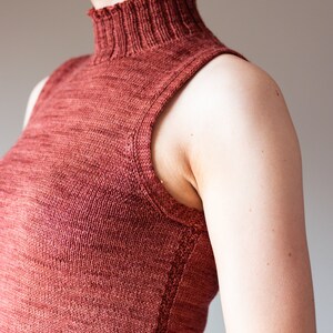 May include: A sleeveless, rust-colored knitted top with a high neck.