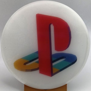May include: A white round coaster with a red, blue, yellow, and black PlayStation logo.