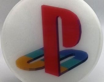 May include: A white round coaster with a red, blue, yellow, and black PlayStation logo.