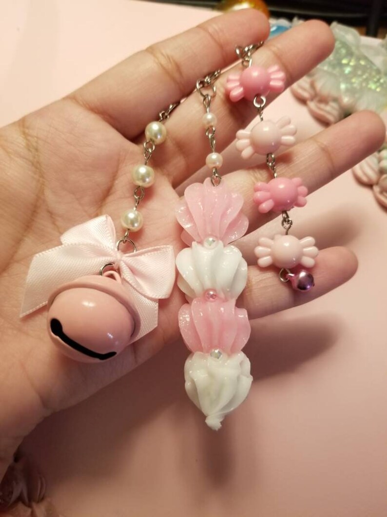 以下が含まれることがあります： ベル、キャンディー、花の形をしたチャームが付いたピンクと白のチャームチェーン2本。