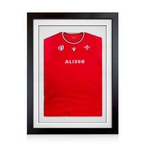 May include: A red sports jersey displayed in a black frame with a white mount. The jersey features a white round neckline, the text ALISON in white, and two white logos on the chest, including the Welsh Prince of Wales feathers emblem.